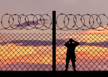 Concept of security. Silhouette of a military border guard and a fence on the background of sunset