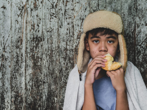 Hungry child eating bread that asking help for food donation from the people on street at the city. Unidentified homeless child begging on street. Shelter concept. Hungry child eating bread that asking help for food donation from the people on street at the city. Unidentified homeless child begging on street. Shelter concept.